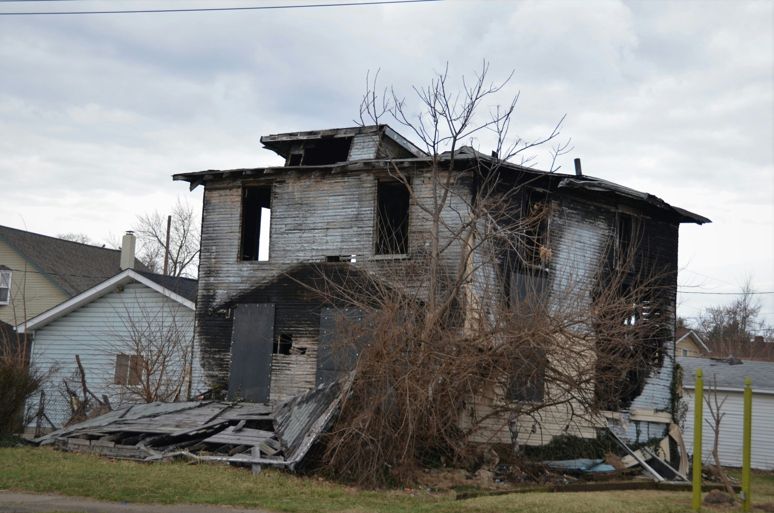 fire_damage Two-story fire-damaged house with charred wood and collapsed roof, debris on the yard.